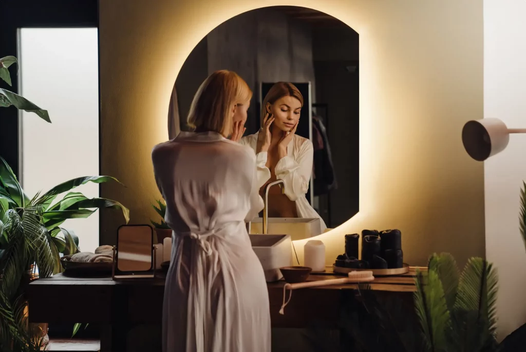 Mujer se maquilla en el baño frente al espejo retroiluminado Wallfluent.